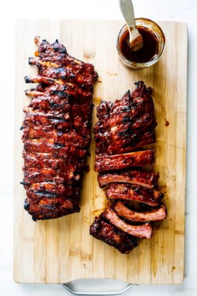 Two racks of bbq ribs with one cut into rib servings with a serving of barbecue sauce on the side