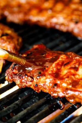 Baby Back Ribs on grill being brushed with bbq sauce