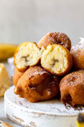 A close up of a banana fritter split open on pile of other fritters