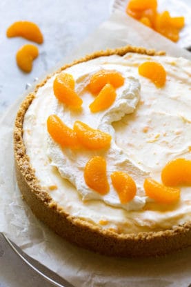 A creamsicle cheesecake sitting on parchment paper with whipped cream and mandarin oranges garnished on top