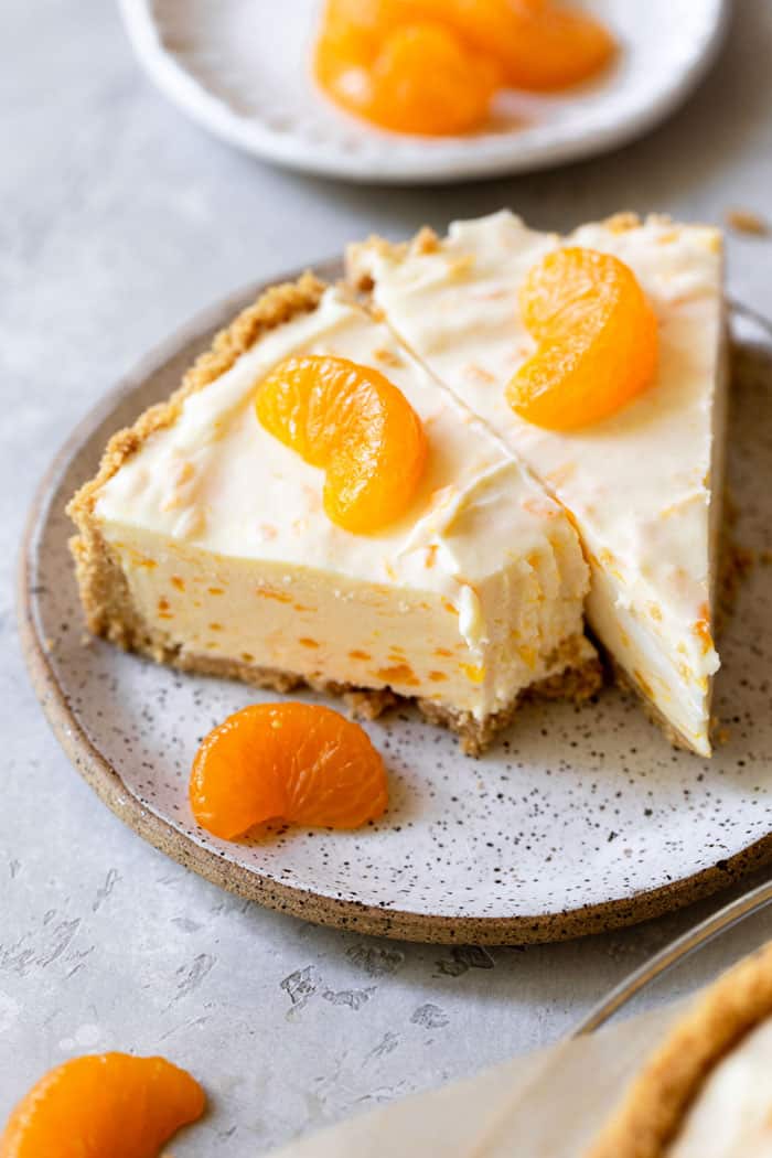 Two slices of creamsicle cheesecake with mandarin oranges garnished on top and on a nearby plate