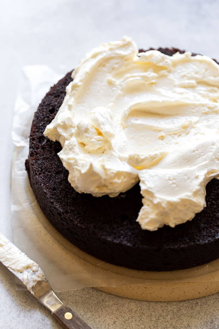 Vanilla buttercream being spread on a layer of chocolate cake