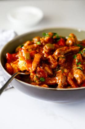 A bowl of grillades with peppers and herbs over a bowl of grits