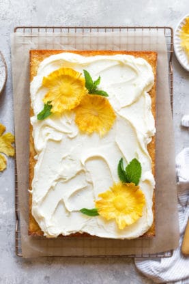 An overhead shot of a large pineapple sheet cake with cream cheese frosting and dried pineapple flowers ready to serve