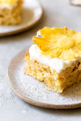 A beautiful close up of a slice of pineapple sheet cake with a dried pineapple on top of white frosting
