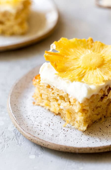 A beautiful close up of a slice of pineapple sheet cake with a dried pineapple on top of white frosting