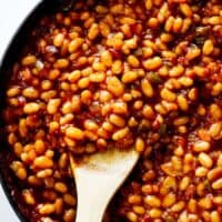 A large wooden spoon serving baked beans in a large skillet