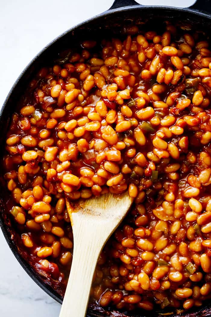 A large wooden spoon serving baked beans in a large skillet