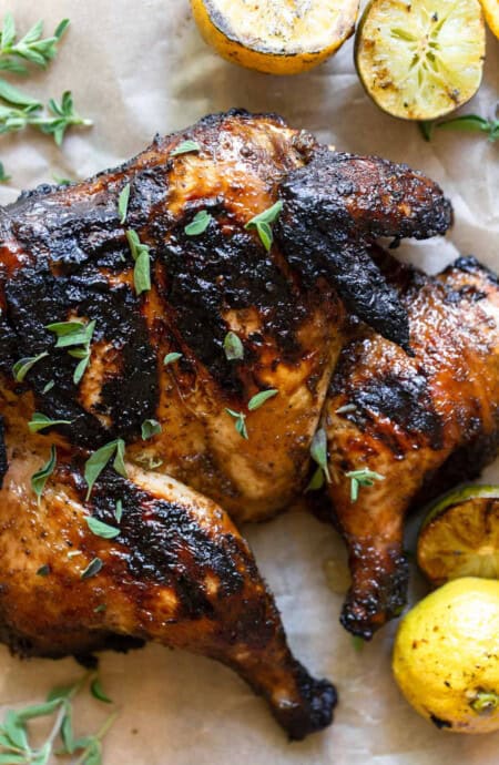 a delicious charred grilled spatchcock chicken sprinkled with herbs next to grilled citrus fruit