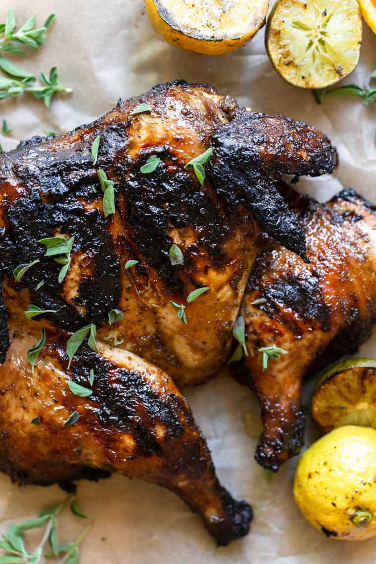 A delicious charred grilled spatchcock chicken sprinkled with herbs next to grilled citrus fruit