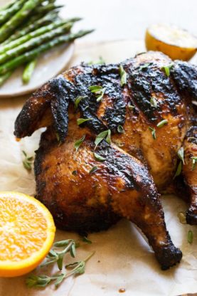 A close up of grilled whole chicken next to grilled fruit and asparagus ready to serve