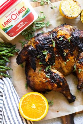 A delicious grilled whole chicken on parchment with lemons, limes, herbs and butter near by