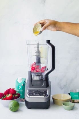 Frozen strawberries in blender with hand pouring liquid in to blend