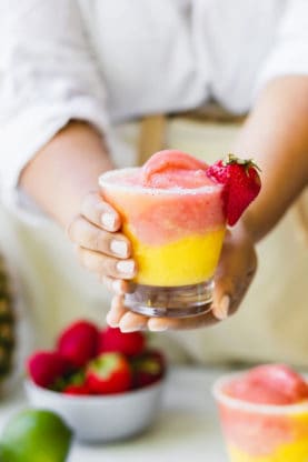 Two hands holding a half strawberry and half mango frozen wine slushy ready to serve