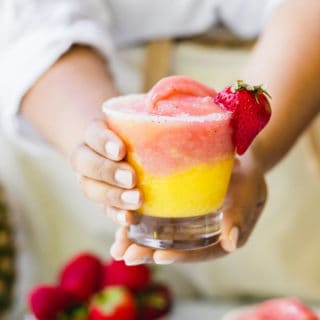 Two hands holding a half strawberry and half mango frozen wine slushy ready to serve