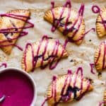 Blueberry turnovers on parchment paper with icing drizzled over them and icing in a bowl