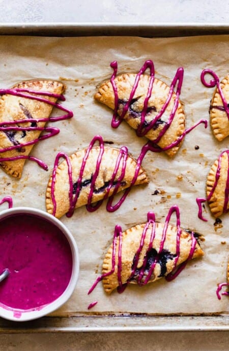 Blueberry turnovers on parchment paper with icing drizzled over them and icing in a bowl