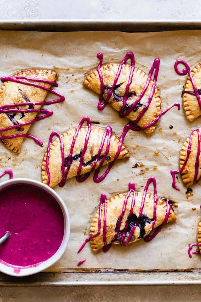 Blueberry turnovers on parchment paper with icing drizzled over them and icing in a bowl