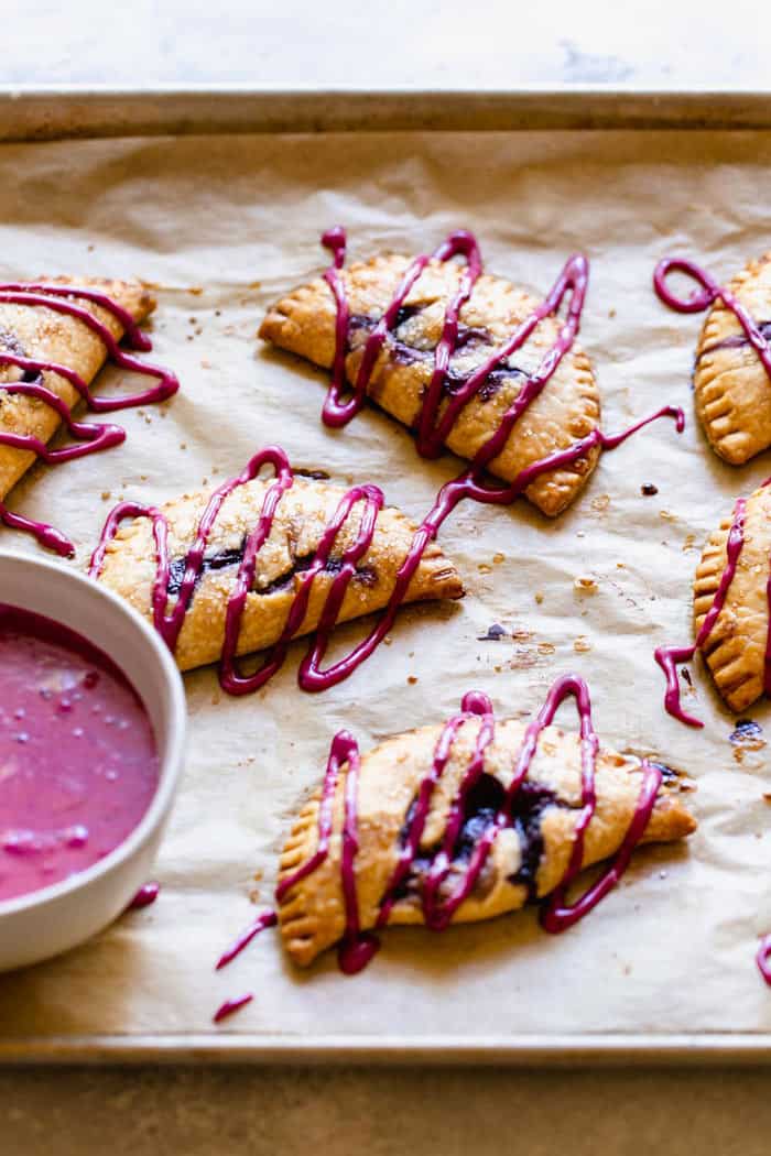 Blueberry hand pies just baked on parchment paper with icing on top