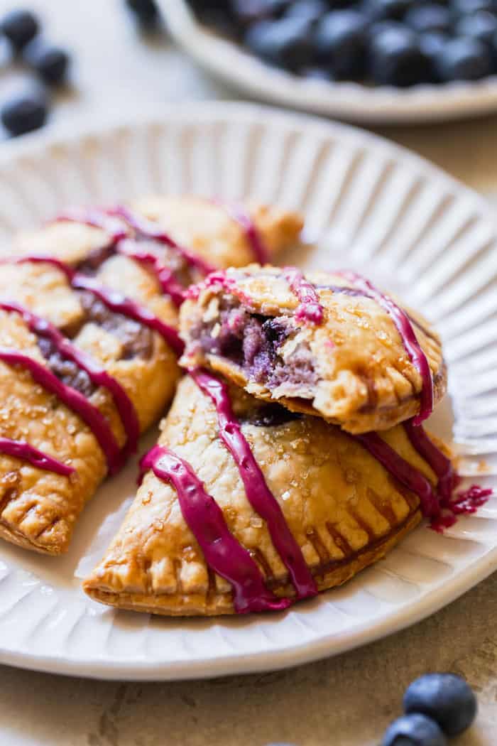 A close up of two blueberry hand pies with one split open showing cream blueberry filling on a white plate