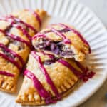 A close up of two blueberry hand pies with one split open showing cream blueberry filling on a white plate