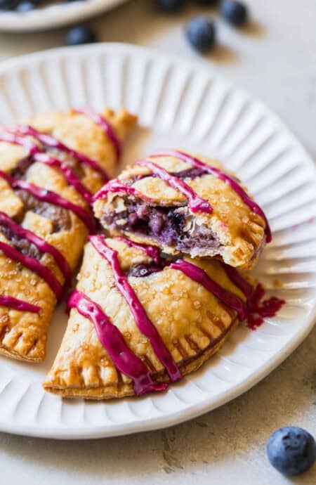 A close up of two blueberry hand pies with one split open showing cream blueberry filling on a white plate