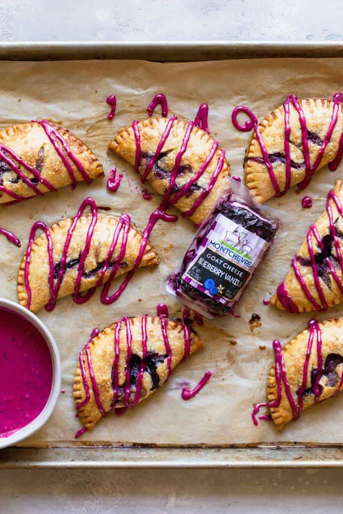 Blueberry hand pies baked on parchment paper with a blueberry drizzle over the tops ready to serve