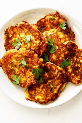A white plate is filled with corn cakes and topped with fresh parsley ready to serve