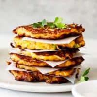 A beautiful stack of corn fritters with parchment paper in between topped with parsley