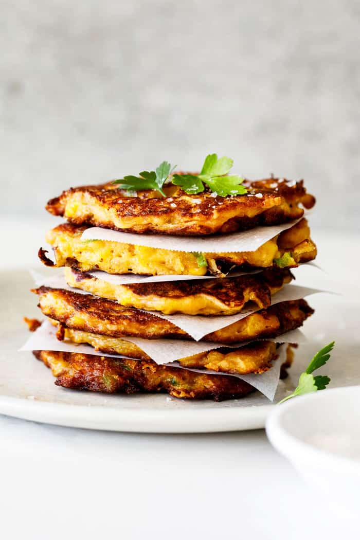A beautiful stack of corn fritters with parchment paper in between topped with parsley
