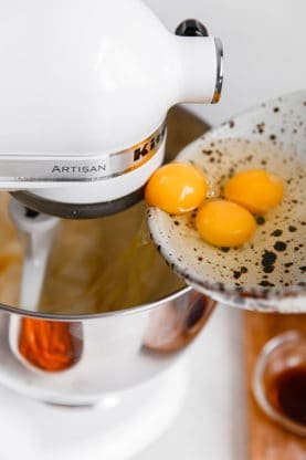 eggs being added to a stand mixer while baking