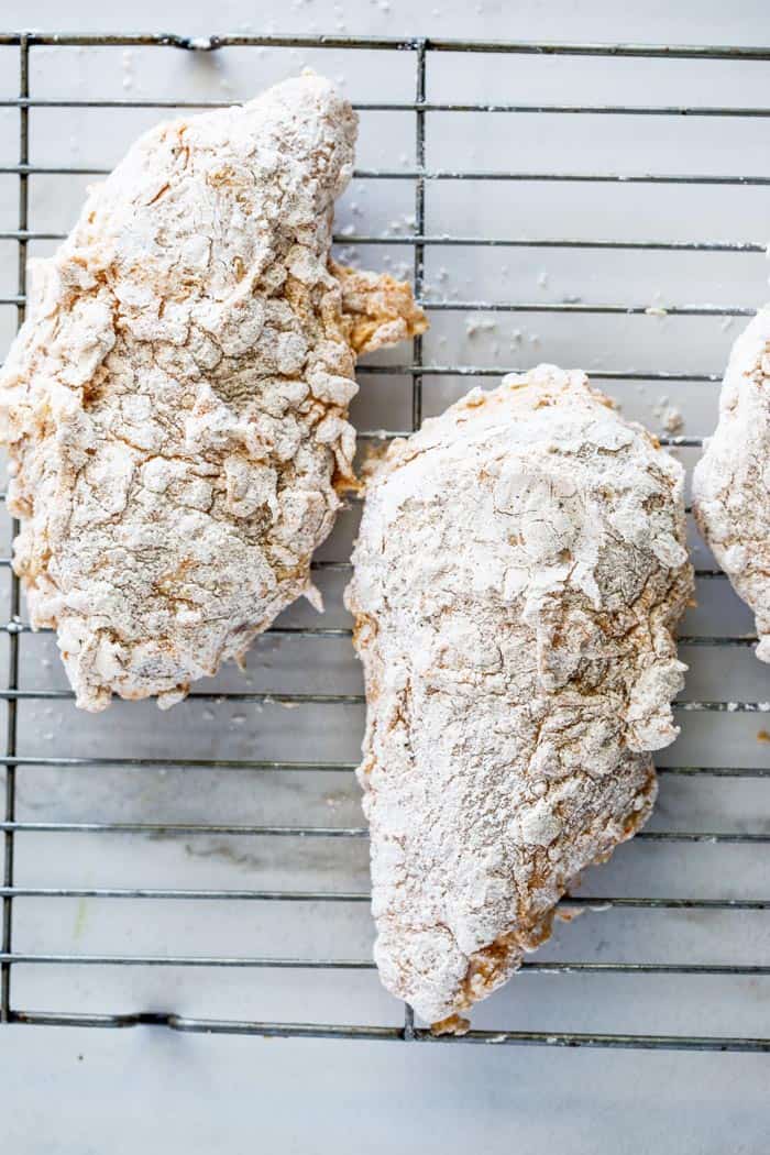 Pieces of skinless chicken breasts that are breaded with flour on wire rack