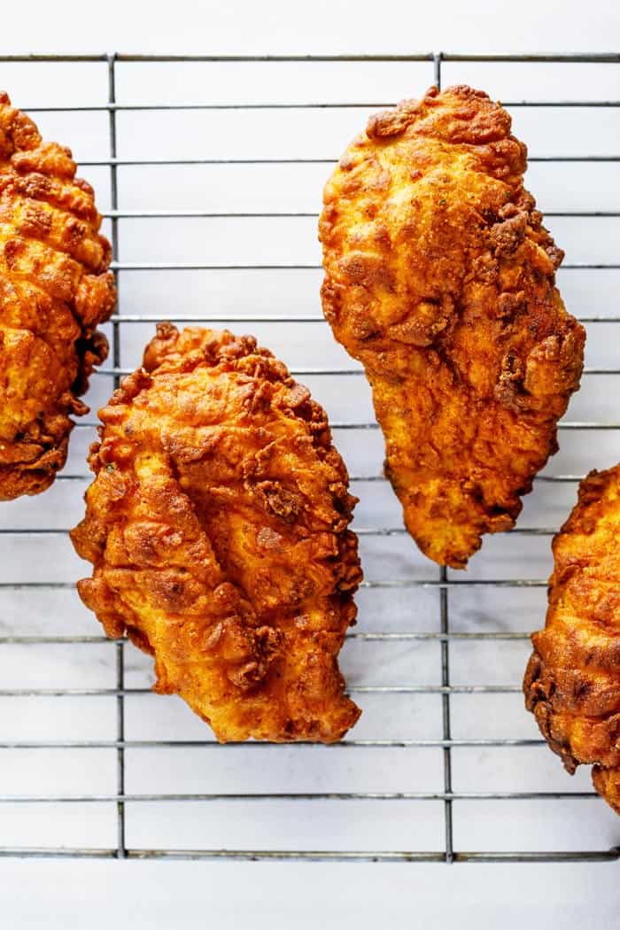 Golden crispy fried chicken breasts on a wire rack draining