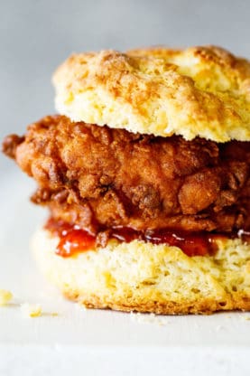 An extreme close up of a golden fried chicken biscuit with red pepper jelly ready to serve