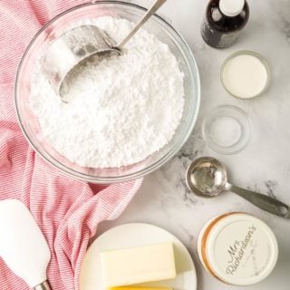 an overhead photo of powdered sugar with a measuring cup, butter, and other ingredients ready to use for baking