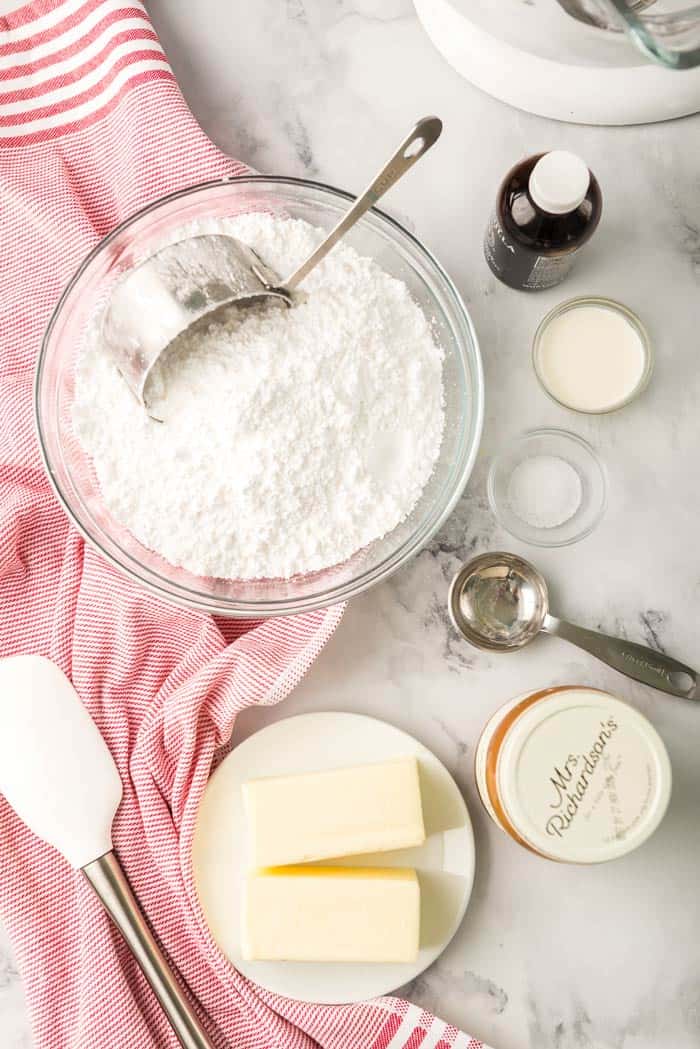 an overhead photo of powdered sugar with a measuring cup, butter, and other ingredients ready to use for baking