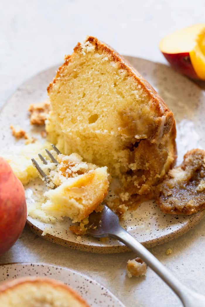 A slice of peach cobbler pound cake with peach filling on a white plate being eaten with a fork