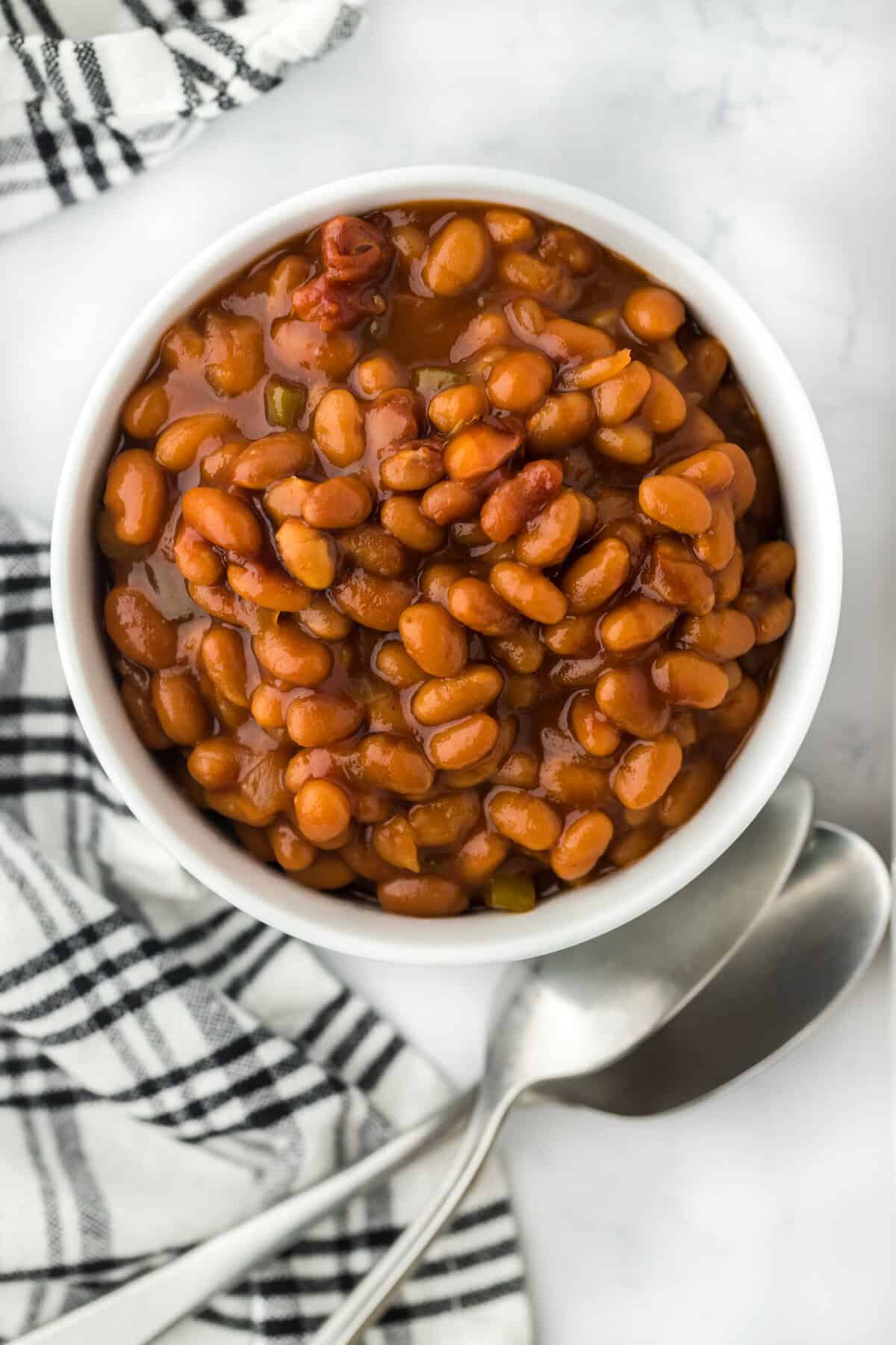 BBQ Baked bean recipe in a white bowl on a white background with black and white striped napkin
