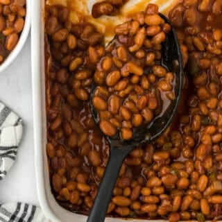 A close up of the best baked beans in a white casserole dish with a spoon scooping some to serve