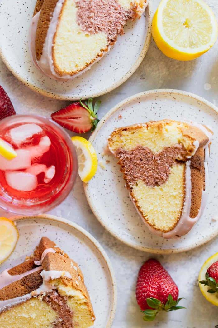 Slices of lemon pound cake with a strawberry swirl in the center with a glass strawberry lemonade with fruit