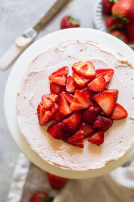 An overhead photo of a strawberry buttercream frosted layer cake with strawberry slices on top