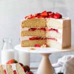 A vanilla cake with strawberry filling sliced with a large slice on a plate with strawberries near by