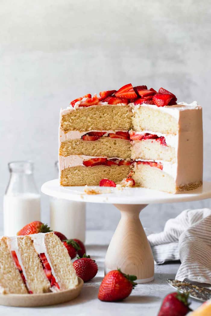 A vanilla cake with strawberry filling sliced with a large slice on a plate with strawberries near by