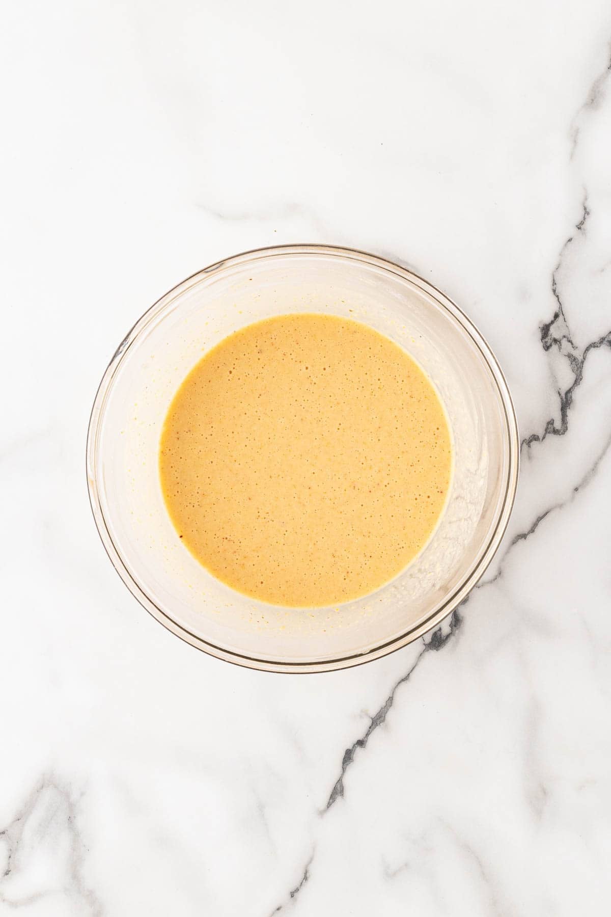 Fritter batter mixed in a glass bowl on a white marble surface