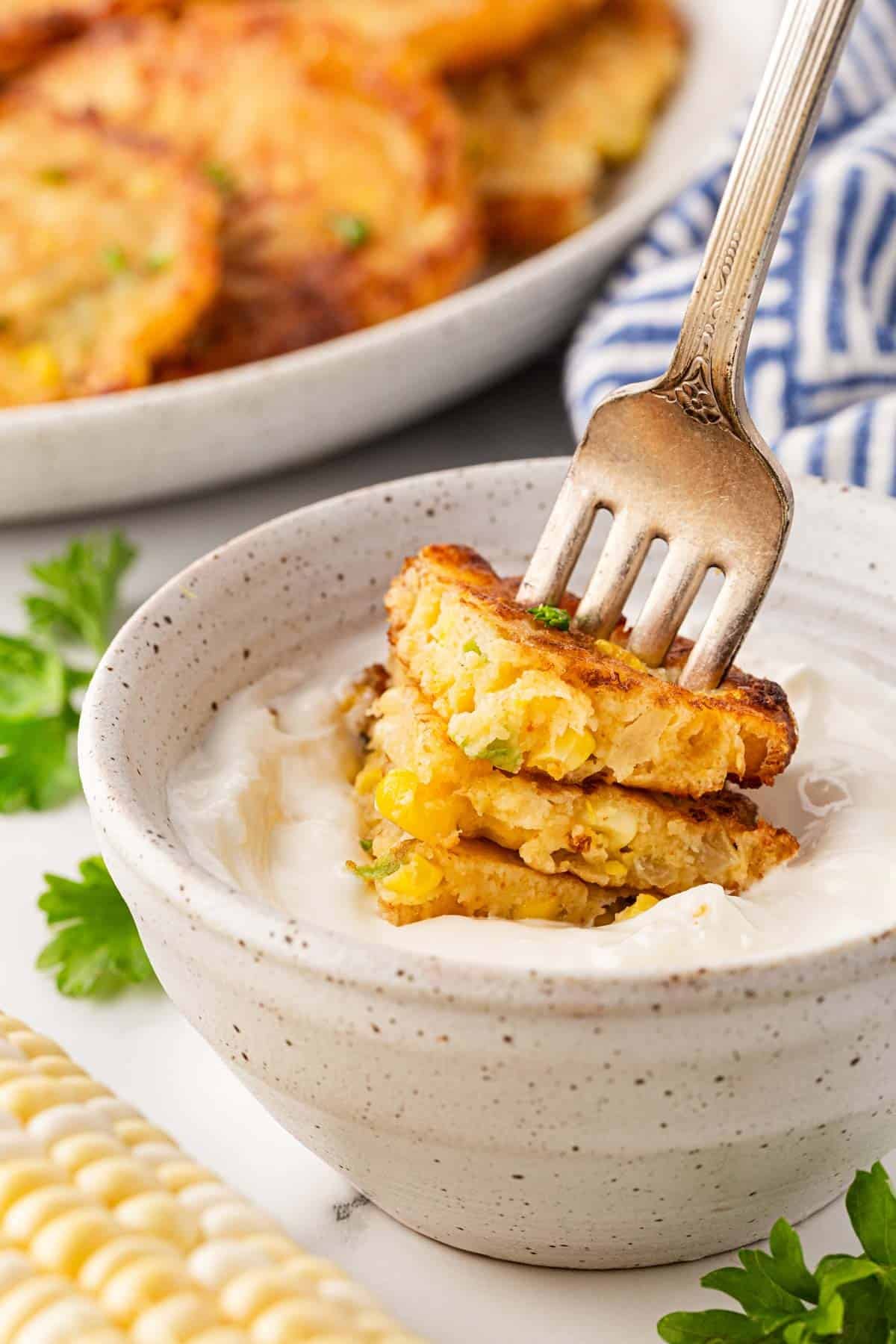 Corn fritter dipped into a bowl of sour cream with a fork