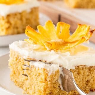 Pineapple cake slice with fork cutting into the frosted cake on a plate