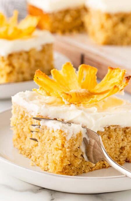 Pineapple cake slice with fork cutting into the frosted cake on a plate
