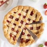 Sliced strawberry pie with one slice removed, surrounded by fresh strawberries, milk, and more pie