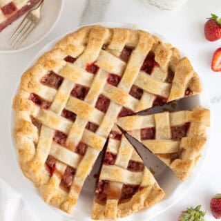 Sliced strawberry pie with one slice removed, surrounded by fresh strawberries, milk, and more pie