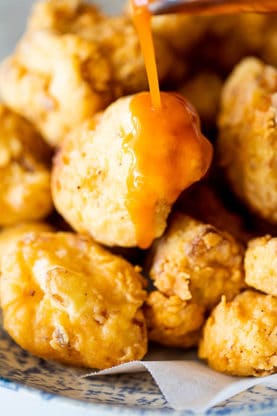 Golden fried cauliflower with buffalo sauce being poured on top to serve